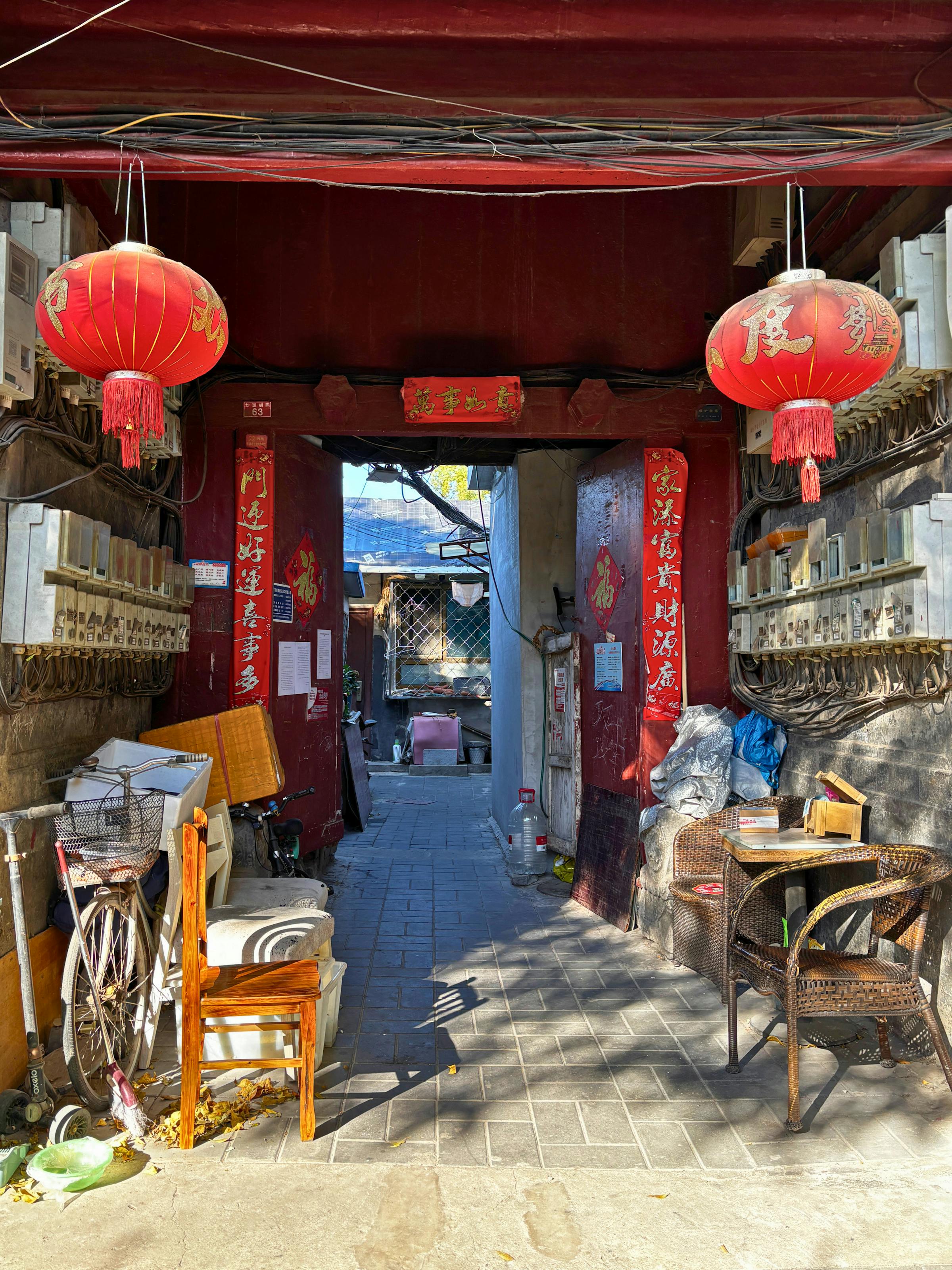 A Beijing hutong alleyway with grey courtyard-house walls and a red-painted wooden door